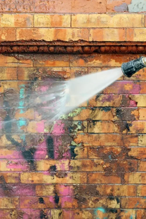 a graffiti on a brick wall being removed with a pressure washer