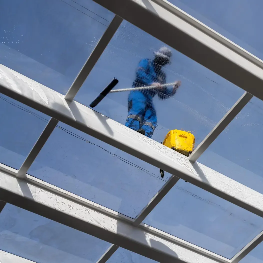 a professional window cleaner stands on and cleans a hotel's glazed conservatory roof