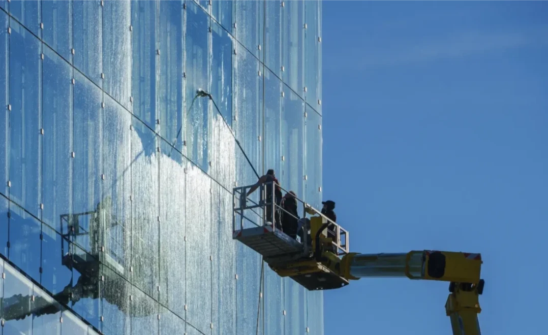 window cleaners on an elevated platform cleaning the glass windows of a London hotel's exterior with a reach and wash system
