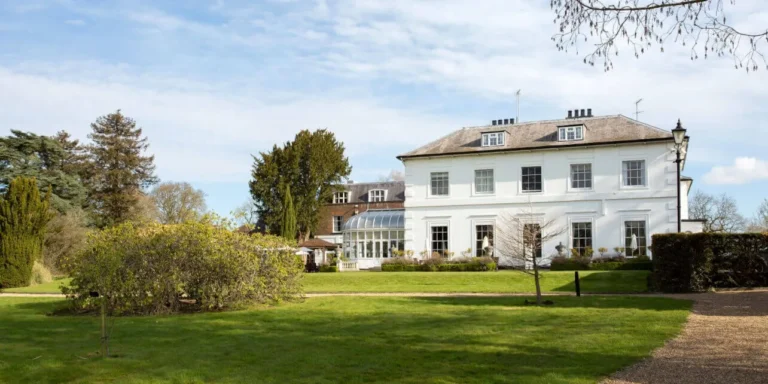 The white Georgian frontage of West Lodge Park hotel, seen across its lawns and arboretum on a clear spring morning.
